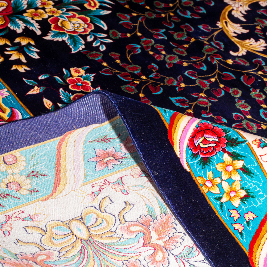 Elegant navy silk rug with detailed floral medallion, ornate cream border, and rich design in gold, coral, and turquoise tones.