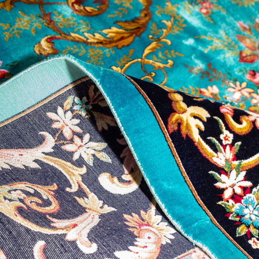 The Archie silk rug in turquoise with red floral motifs and golden scrolls, featuring a black ornamental border and exquisite handwoven detailing.