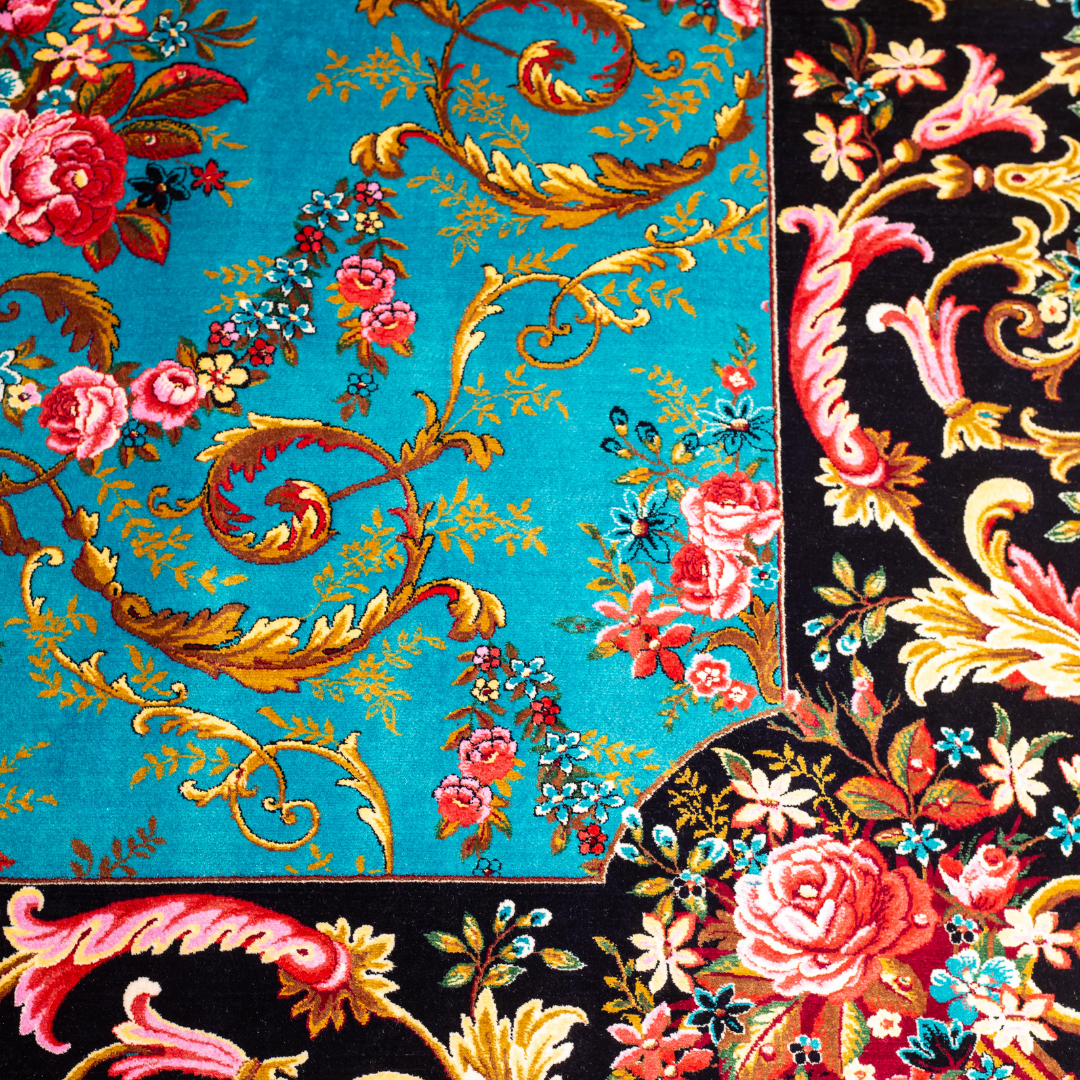 The Archie silk rug in turquoise with red floral motifs and golden scrolls, featuring a black ornamental border and exquisite handwoven detailing.
