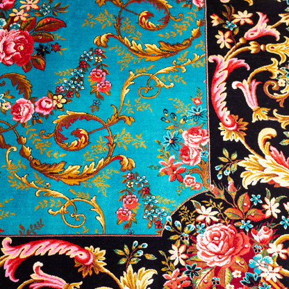 The Archie silk rug in turquoise with red floral motifs and golden scrolls, featuring a black ornamental border and exquisite handwoven detailing.