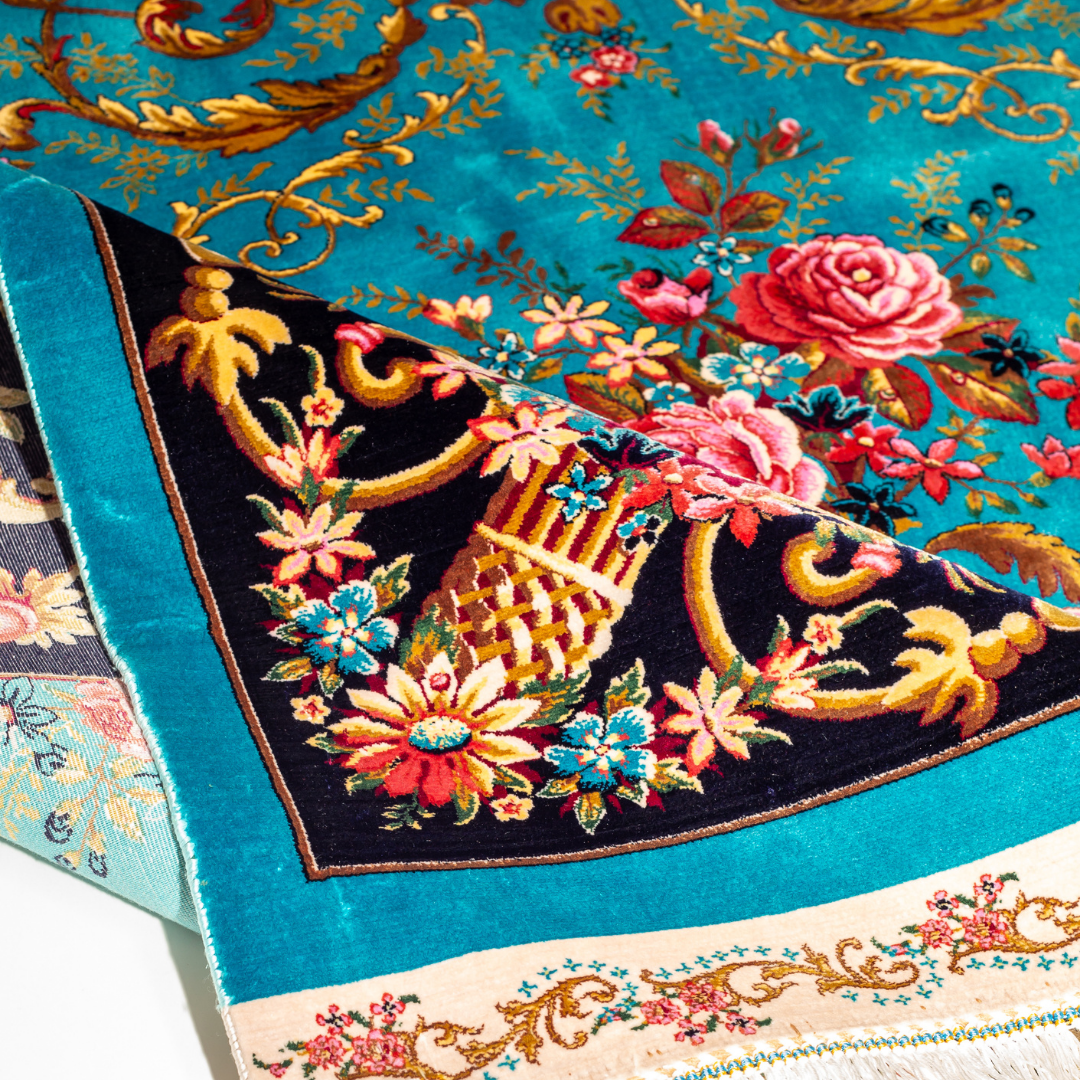 The Archie silk rug in turquoise with red floral motifs and golden scrolls, featuring a black ornamental border and exquisite handwoven detailing.