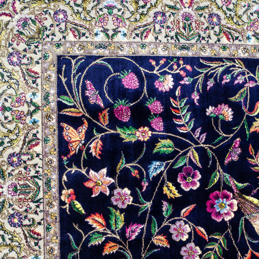 Navy silk rug with floral, bird, and vine motifs in pink, green, and multicolour tones, bordered in ivory.

