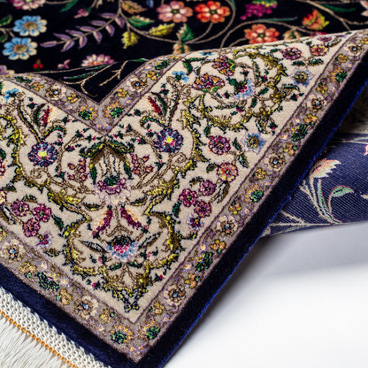 Navy silk rug with floral, bird, and vine motifs in pink, green, and multicolour tones, bordered in ivory.

