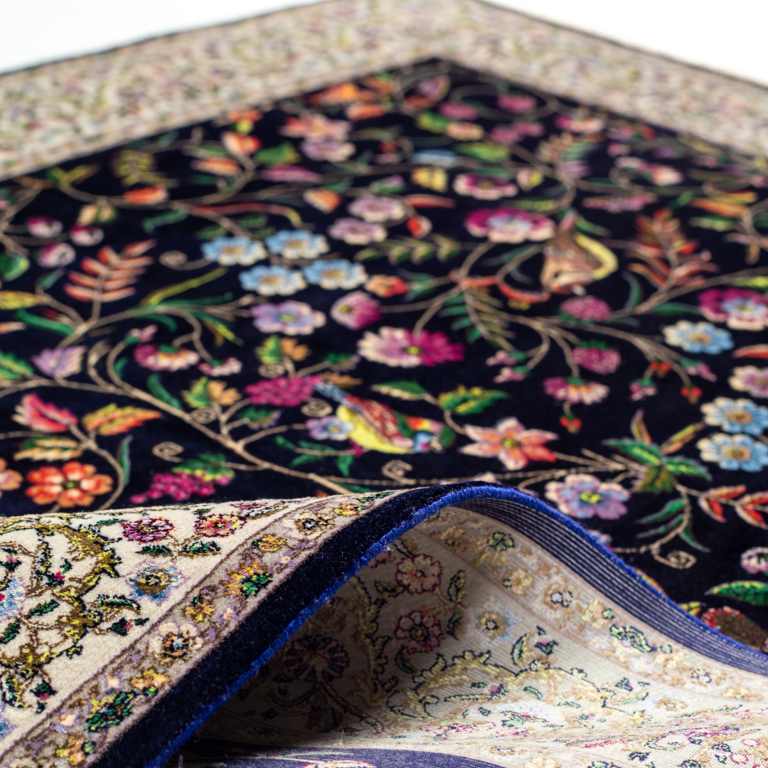 Navy silk rug with floral, bird, and vine motifs in pink, green, and multicolour tones, bordered in ivory.

