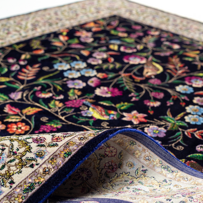 Navy silk rug with floral, bird, and vine motifs in pink, green, and multicolour tones, bordered in ivory.

