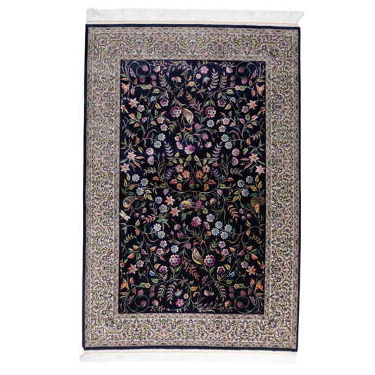 Navy silk rug with floral, bird, and vine motifs in pink, green, and multicolour tones, bordered in ivory.

