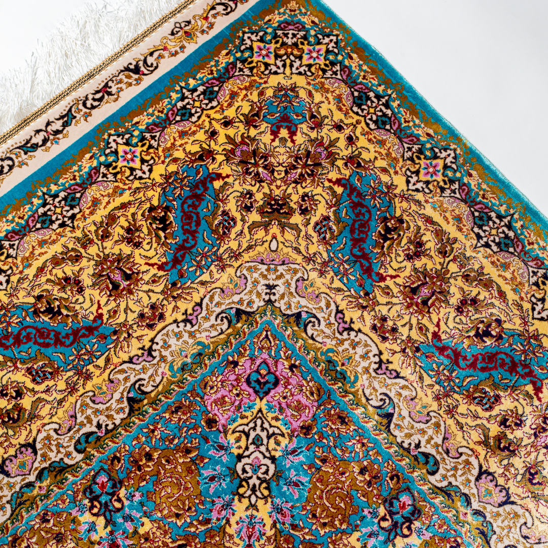 Intricately handwoven silk rug with medallion design, turquoise base, and ornate gold-maroon border for elegant interior styling.

