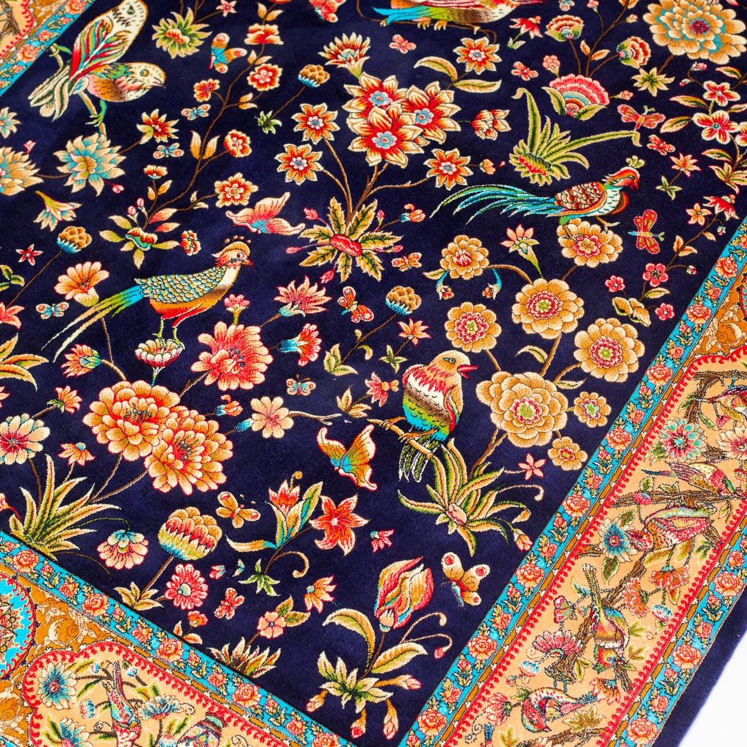 Eden silk rug featuring navy base with multi-colour florals and birds, hand-finished with detailed borders.
