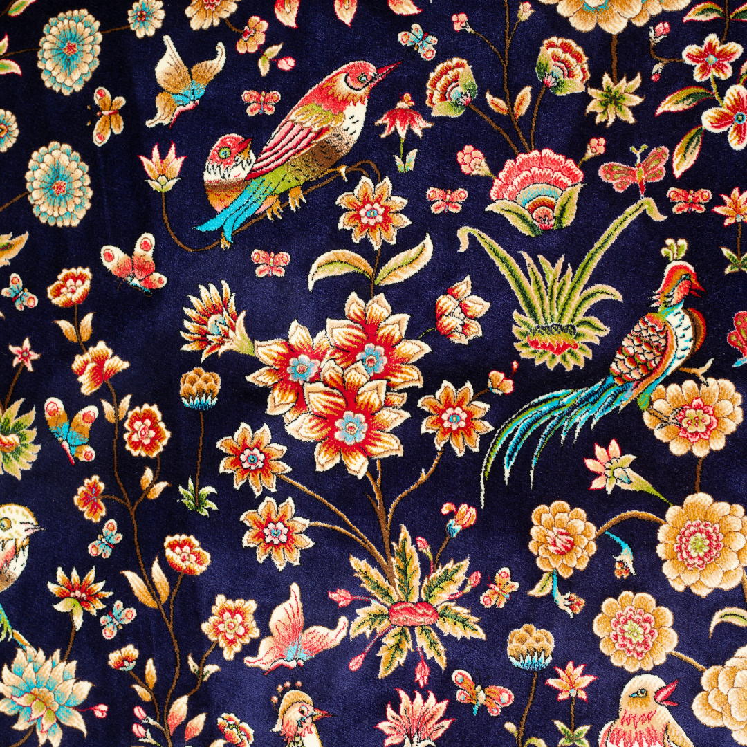 Eden silk rug featuring navy base with multi-colour florals and birds, hand-finished with detailed borders.
