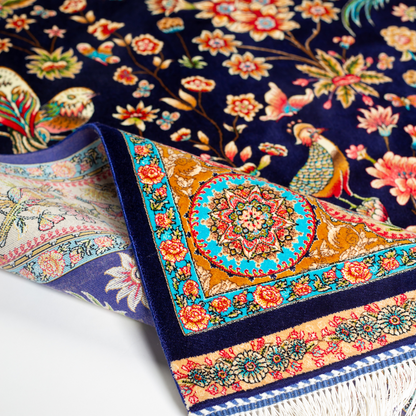Eden silk rug featuring navy base with multi-colour florals and birds, hand-finished with detailed borders.
