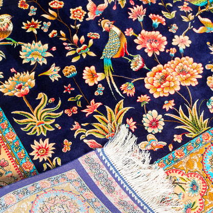 Eden silk rug featuring navy base with multi-colour florals and birds, hand-finished with detailed borders.
