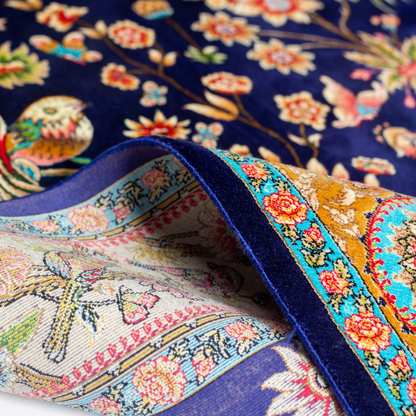 Eden silk rug featuring navy base with multi-colour florals and birds, hand-finished with detailed borders.

