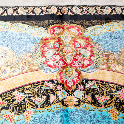 Luxury blue silk rug featuring a detailed central medallion, floral motifs, and ornate bird patterns in gold, coral, and black accents.