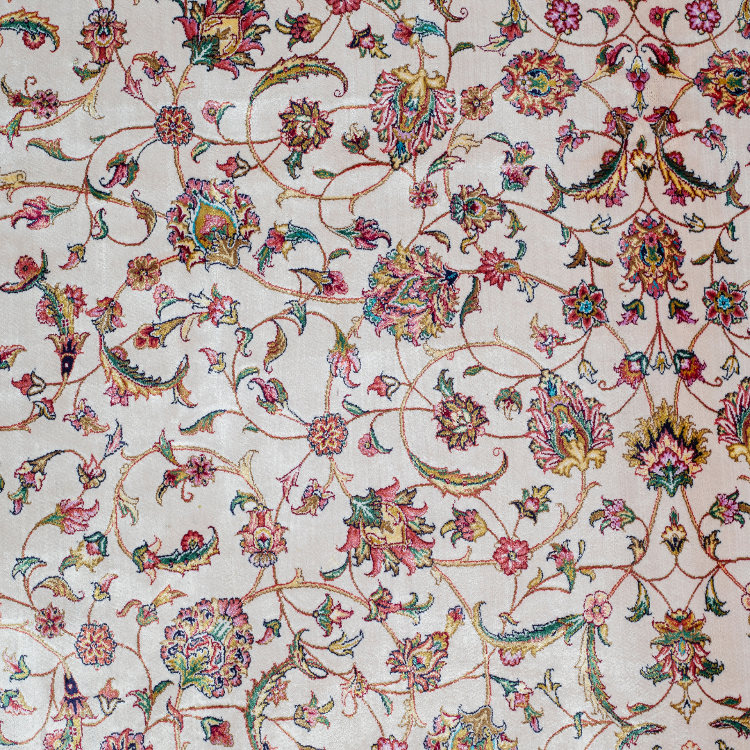 Ivory silk rug with intricate floral patterns in navy, rose, gold, and turquoise, framed with an ornate navy border.


