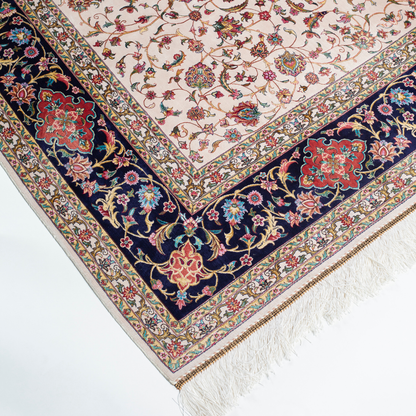 Ivory silk rug with intricate floral patterns in navy, rose, gold, and turquoise, framed with an ornate navy border.



