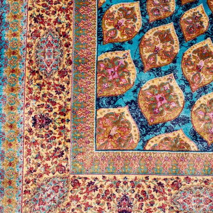 Maki silk rug featuring a turquoise blue base with intricate gold, ruby red, ivory, and fuchsia floral medallion design in a symmetrical pattern.
