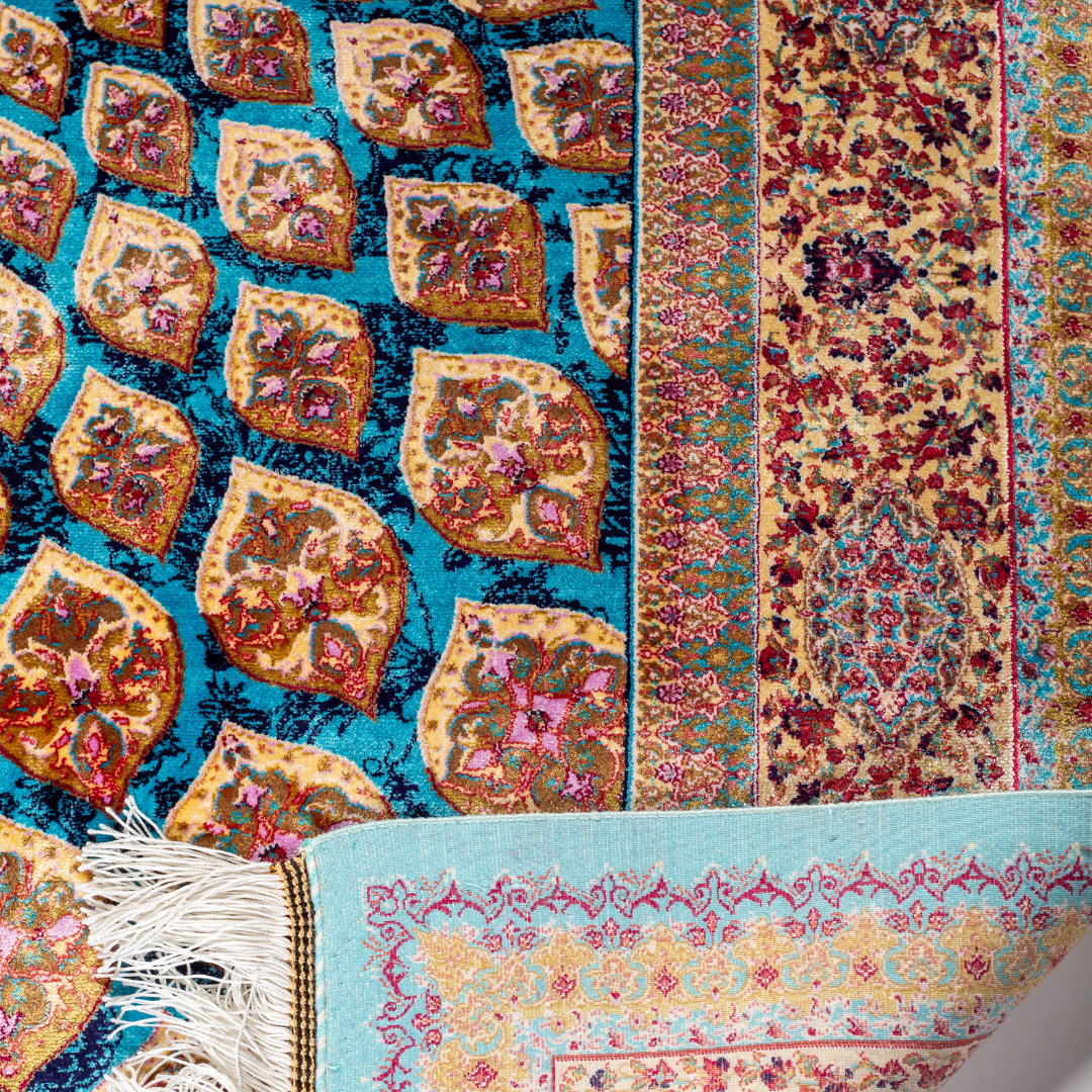 Maki silk rug featuring a turquoise blue base with intricate gold, ruby red, ivory, and fuchsia floral medallion design in a symmetrical pattern.
