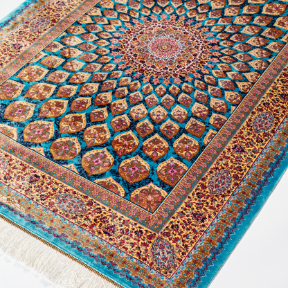 Maki silk rug featuring a turquoise blue base with intricate gold, ruby red, ivory, and fuchsia floral medallion design in a symmetrical pattern.
