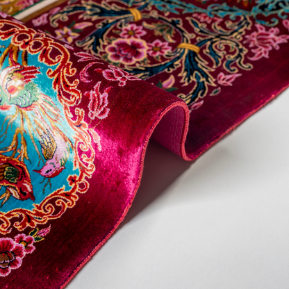 Opulent silk rug with ruby base and turquoise floral accents. Detailed handwoven artistry ideal for luxury, dramatic interior settings.

