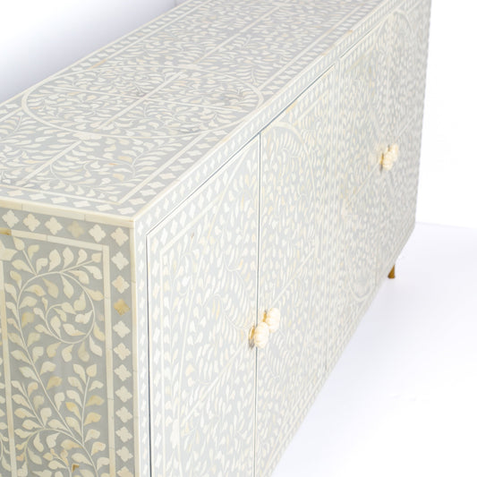 Grey bone inlay cabinet with floral vine pattern, brass legs, and carved bone knobs, handcrafted with spacious storage and artisanal charm.