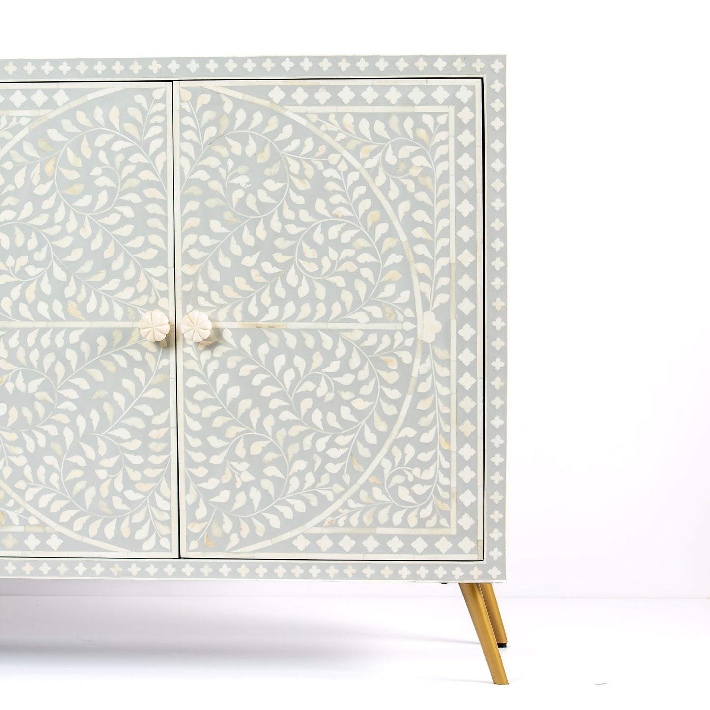 Grey bone inlay cabinet with floral vine pattern, brass legs, and carved bone knobs, handcrafted with spacious storage and artisanal charm.