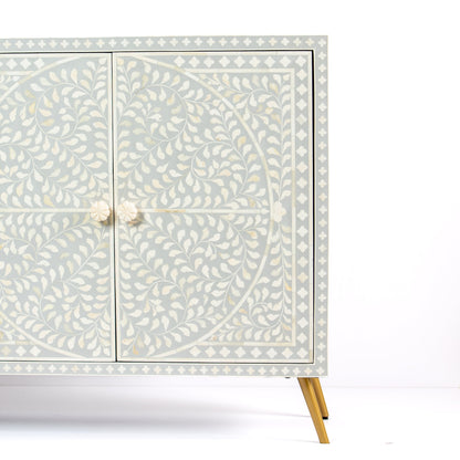 Grey bone inlay cabinet with floral vine pattern, brass legs, and carved bone knobs, handcrafted with spacious storage and artisanal charm.