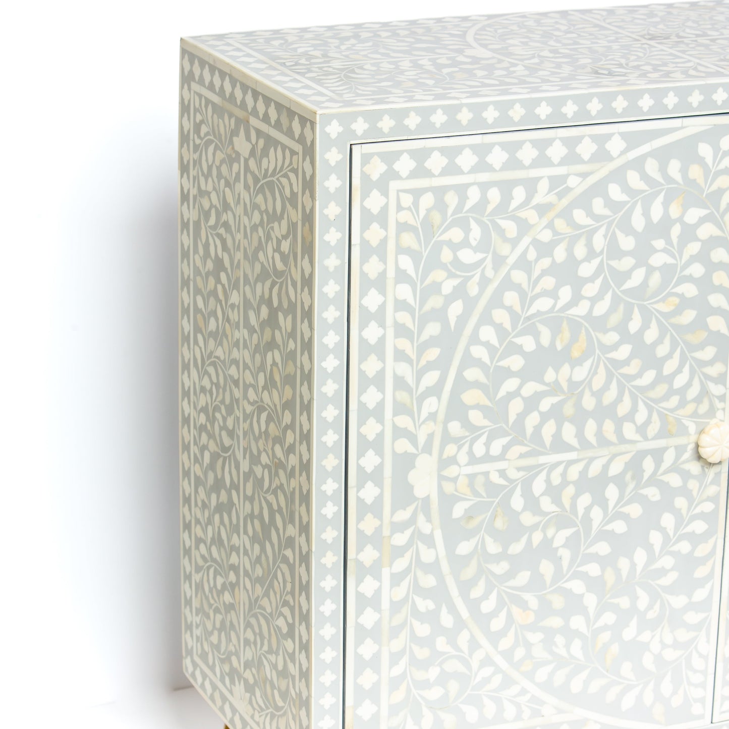 Grey bone inlay cabinet with floral vine pattern, brass legs, and carved bone knobs, handcrafted with spacious storage and artisanal charm.
