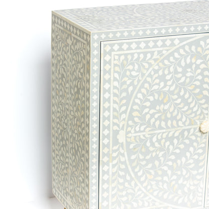 Grey bone inlay cabinet with floral vine pattern, brass legs, and carved bone knobs, handcrafted with spacious storage and artisanal charm.