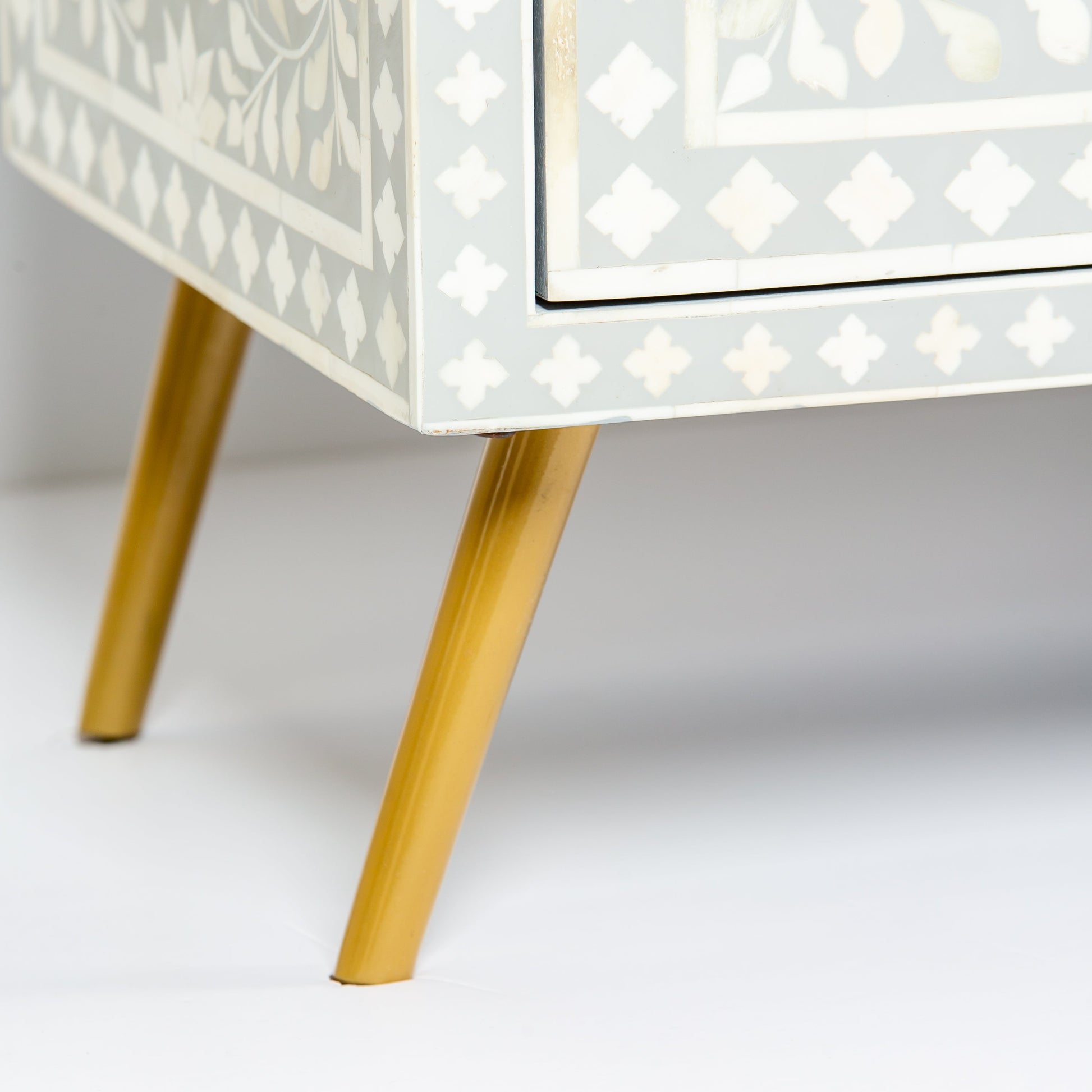 Grey bone inlay cabinet with floral vine pattern, brass legs, and carved bone knobs, handcrafted with spacious storage and artisanal charm.