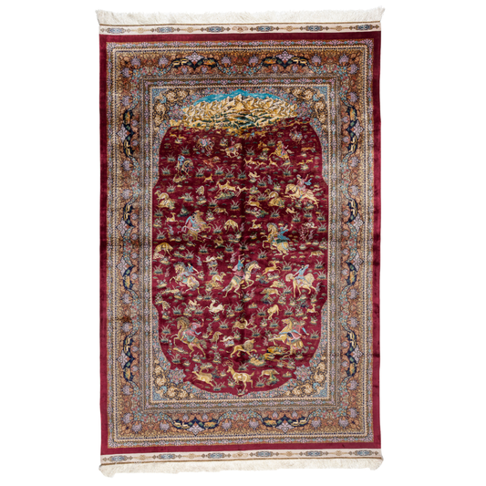 Silk rug in deep garnet red with majestic horsemen, animals, and ornate border work. Handwoven art that brings dynamic motion to interiors.

