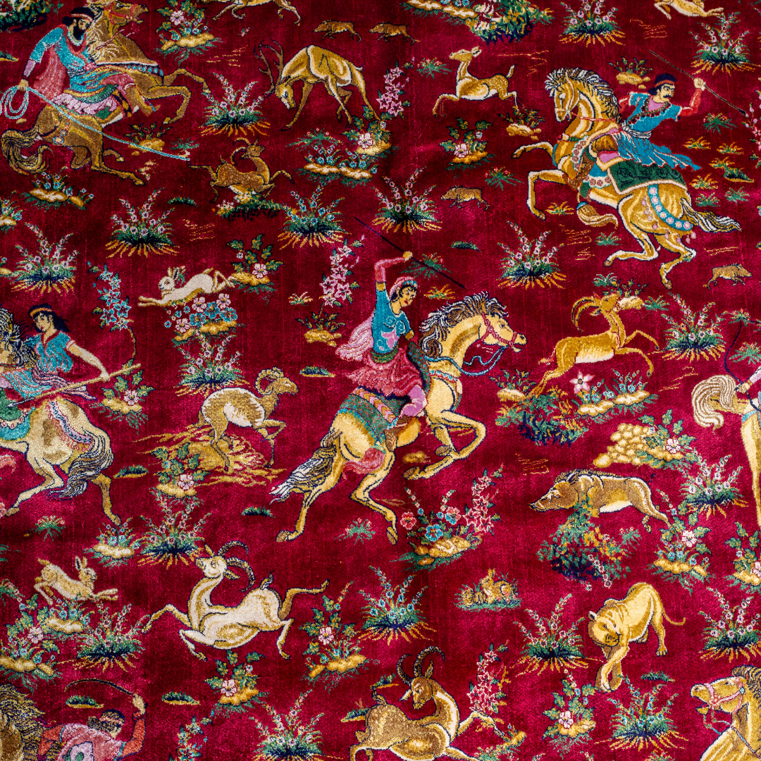 Silk rug in deep garnet red with majestic horsemen, animals, and ornate border work. Handwoven art that brings dynamic motion to interiors.

