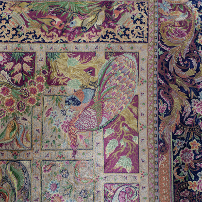 Luxurious silk rug with central bird tree, bordered by peacocks and florals. Handwoven in soft jewel tones with ornate framed details.

