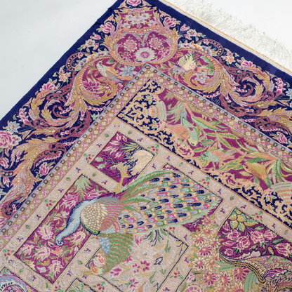 Luxurious silk rug with central bird tree, bordered by peacocks and florals. Handwoven in soft jewel tones with ornate framed details.

