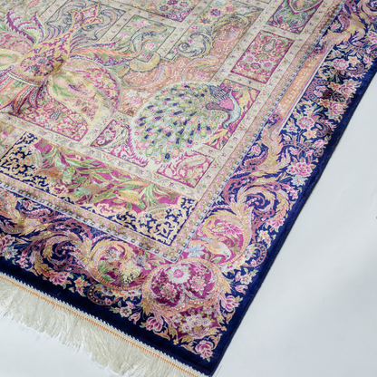 Luxurious silk rug with central bird tree, bordered by peacocks and florals. Handwoven in soft jewel tones with ornate framed details.


