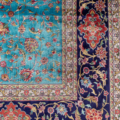 Aquamarine silk rug with coral and ivory floral motifs, framed by an indigo border. Handwoven with intricate detail and radiant sheen.


