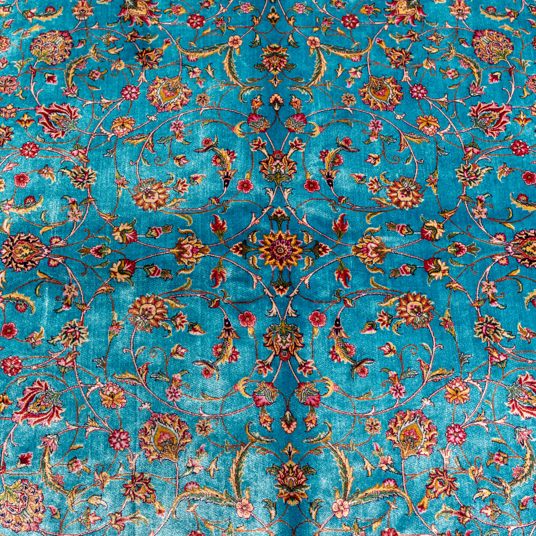Aquamarine silk rug with coral and ivory floral motifs, framed by an indigo border. Handwoven with intricate detail and radiant sheen.

