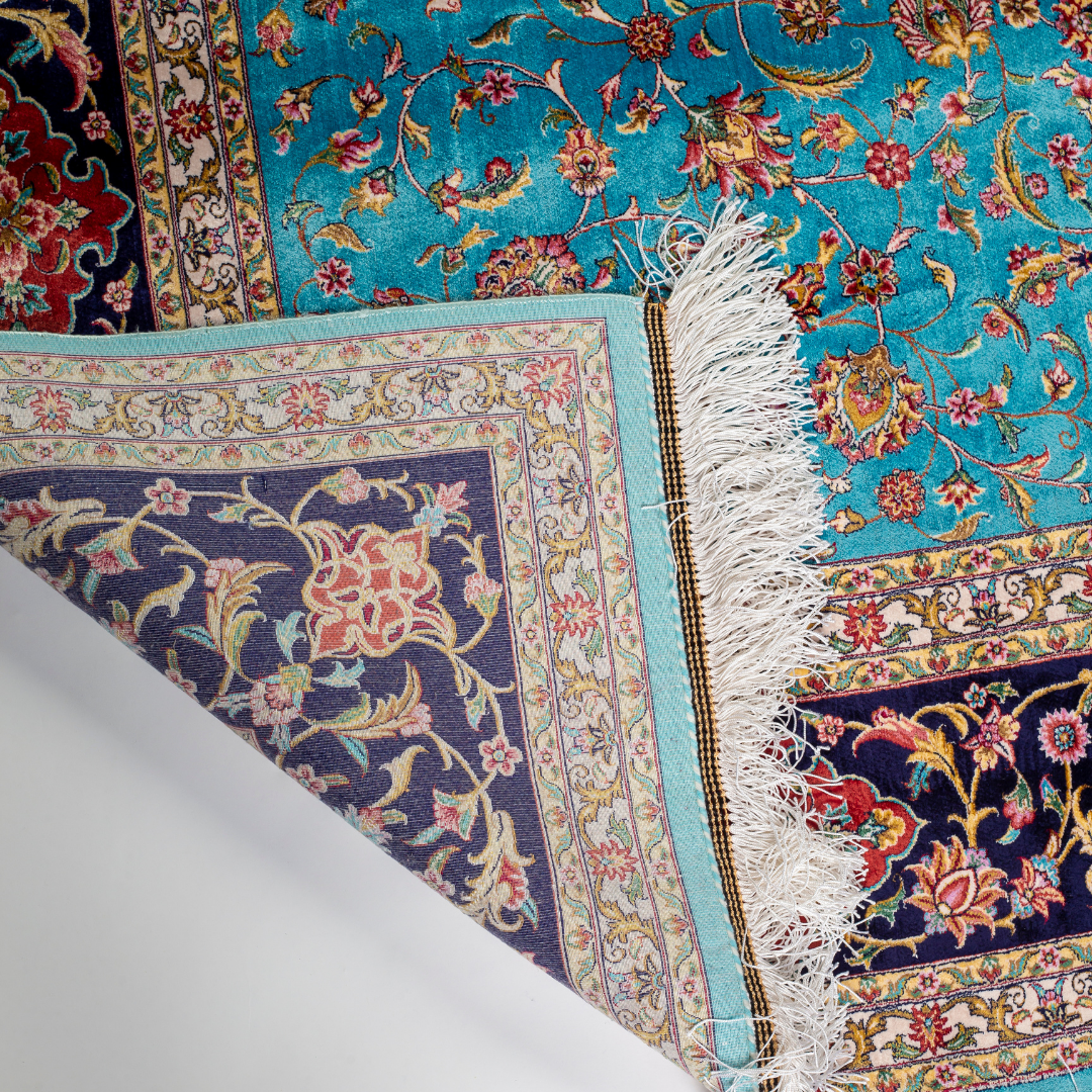 Aquamarine silk rug with coral and ivory floral motifs, framed by an indigo border. Handwoven with intricate detail and radiant sheen.


