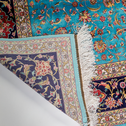 Aquamarine silk rug with coral and ivory floral motifs, framed by an indigo border. Handwoven with intricate detail and radiant sheen.

