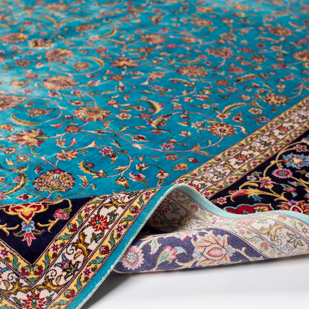 Aquamarine silk rug with coral and ivory floral motifs, framed by an indigo border. Handwoven with intricate detail and radiant sheen.

