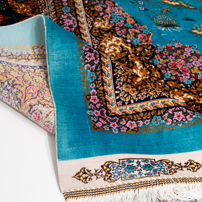 Vibrant handwoven silk rug with a turquoise base, animal motifs, hunting scenes, and floral detailing in gold and pink tones.