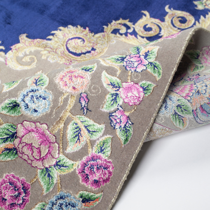 Luxurious silk rug with peacock pair and blooming florals on a navy base. Handwoven in soft hues with intricate botanical detailing.

