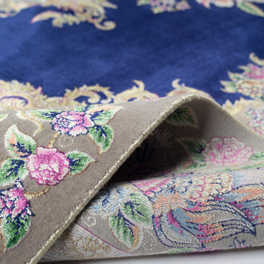 Luxurious silk rug with peacock pair and blooming florals on a navy base. Handwoven in soft hues with intricate botanical detailing.

