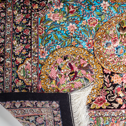 Close-up of the Veo Persian silk rug featuring a floral and bird pattern in navy, turquoise, and gold tones. 150x100 cm size.
