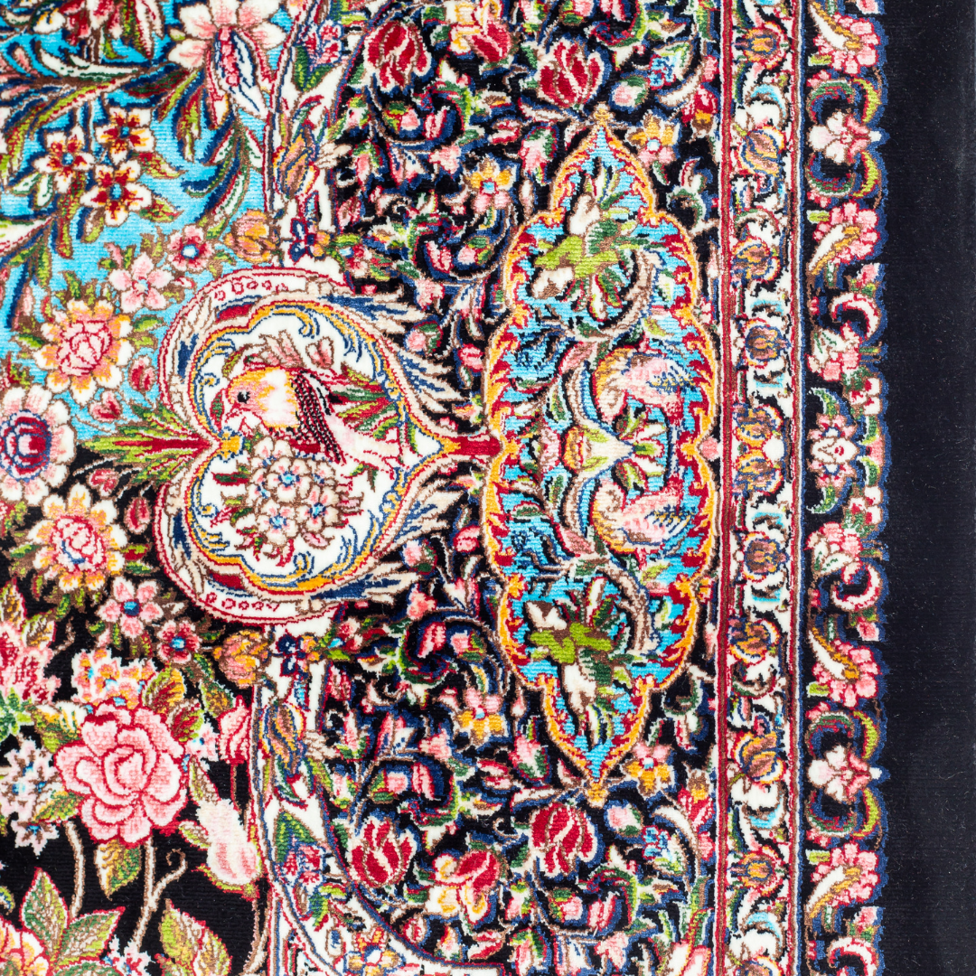 Close-up of the Veo Persian silk rug featuring a floral and bird pattern in navy, turquoise, and gold tones. 150x100 cm size.
